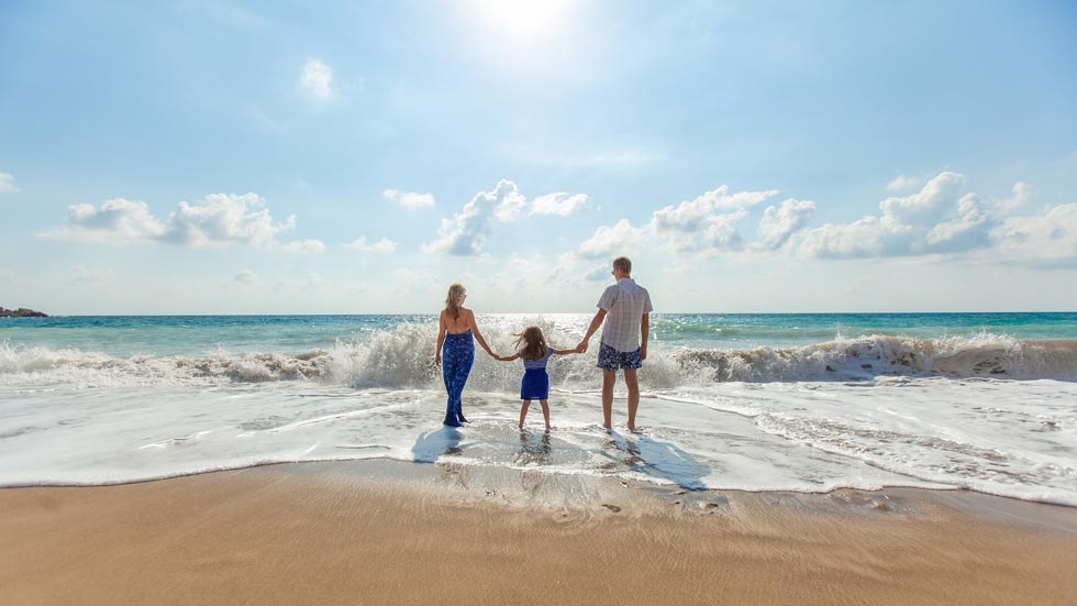 Casal com filho fotografados na praia ao meio-dia.